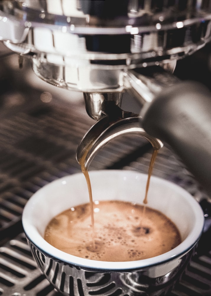 Espresso pour poster with coffee streaming from a machine into a cup
