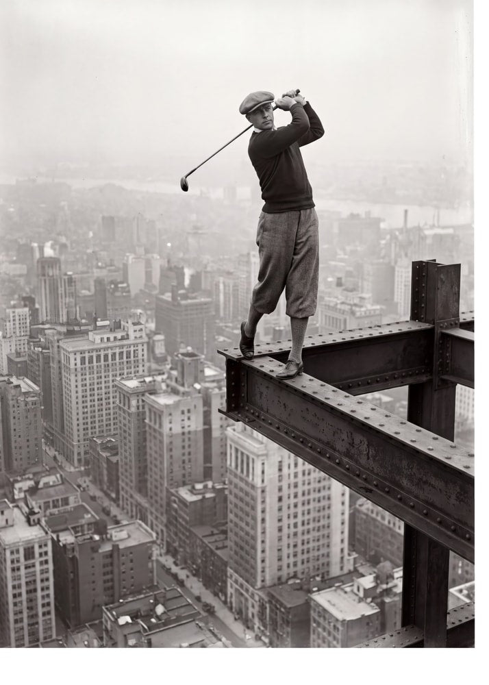 Golfer on beam poster with a black and white view of a man golfing on a steel beam above the city