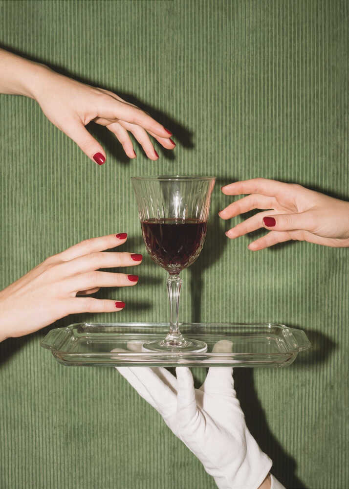 Hands wine glass poster with hands reaching toward a wine glass on a tray held by a gloved hand